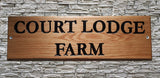 A personalized oak house number name sign, crafted by LD Trade, is mounted on a stone wall. This outdoor wooden plaque features engraved text "COURT LODGE FARM" in black capital letters.