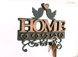 A wall-mounted decorative key holder from LD Trade is displayed against a white wall, showcasing the word "HOME" with two birds kissing above it. Below are heart-shaped hooks, and a set of keys hangs from one hook, ensuring you'll never misplace your keys again. This charming piece is part of the Wall Key Holder Decorative Home Accessories collection.